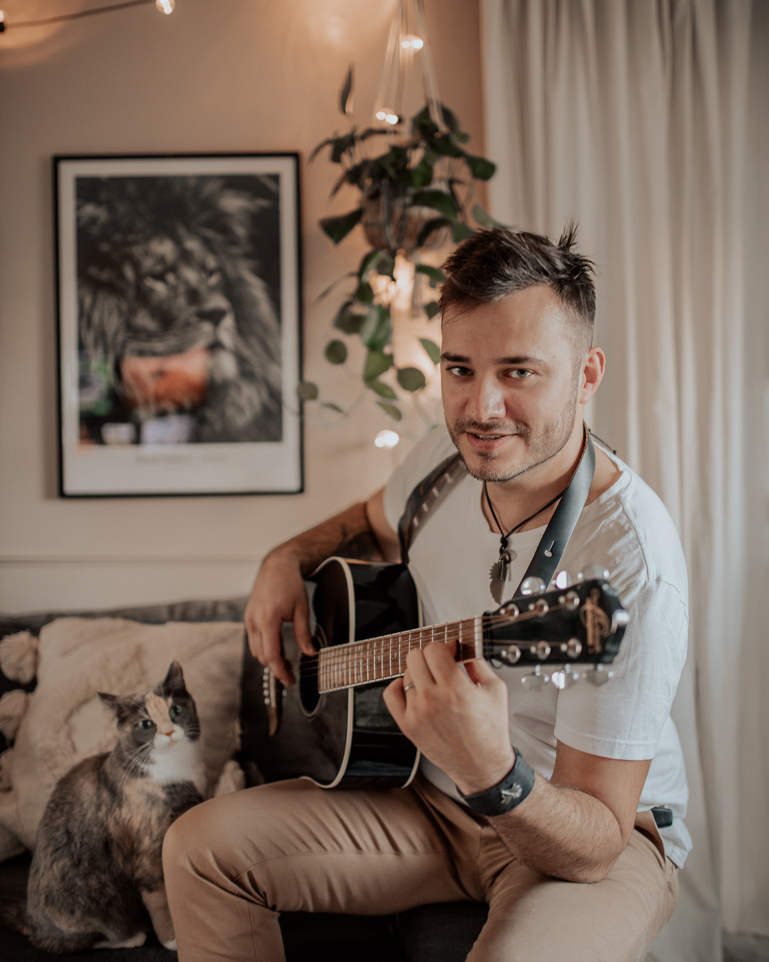 Man playing guitar at home with a cat by his side