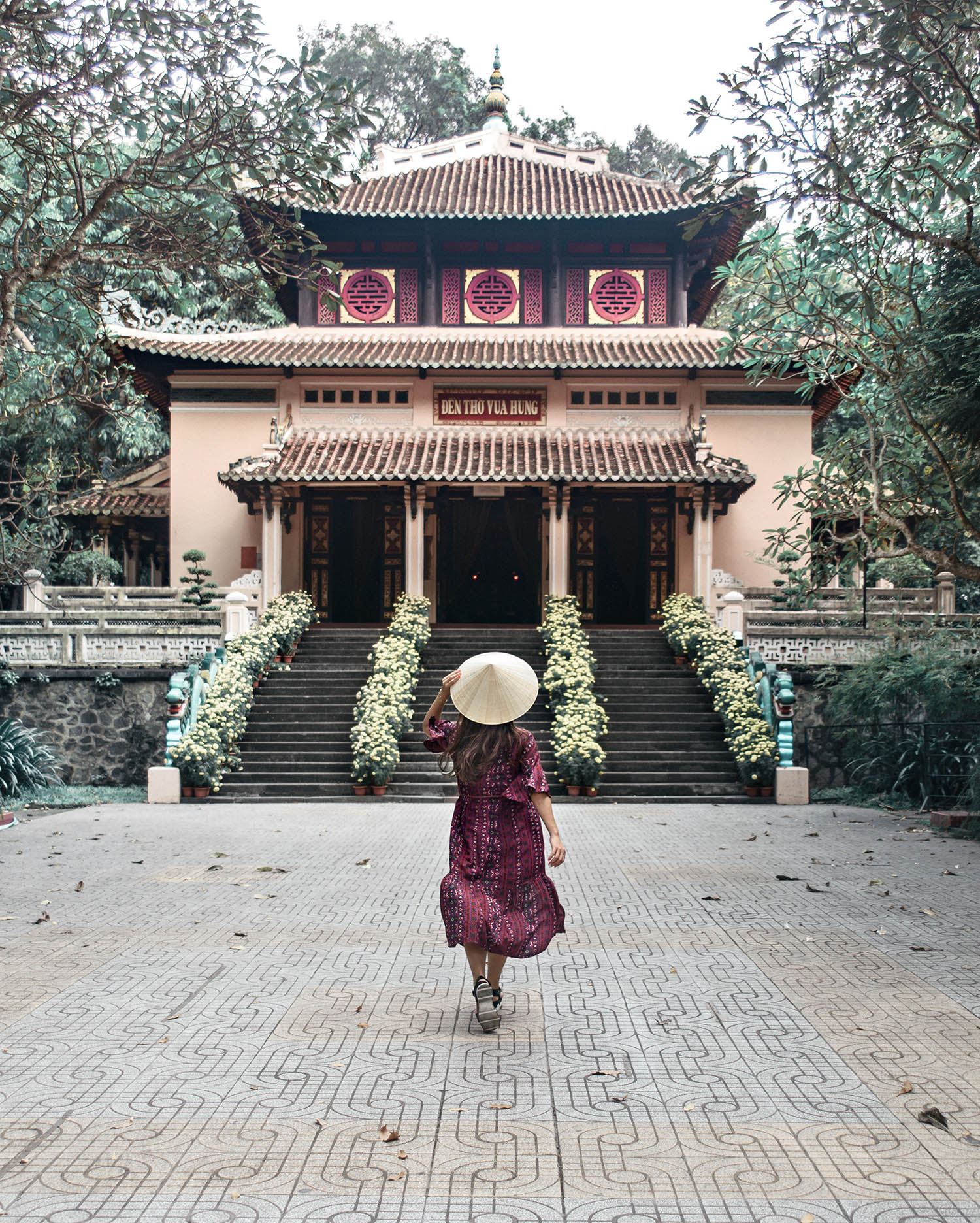 Tjej med rishatt gåendes mot Buddhist templet Đền Thờ Vua Hùng i Ho Chi Minh City, Vietnam