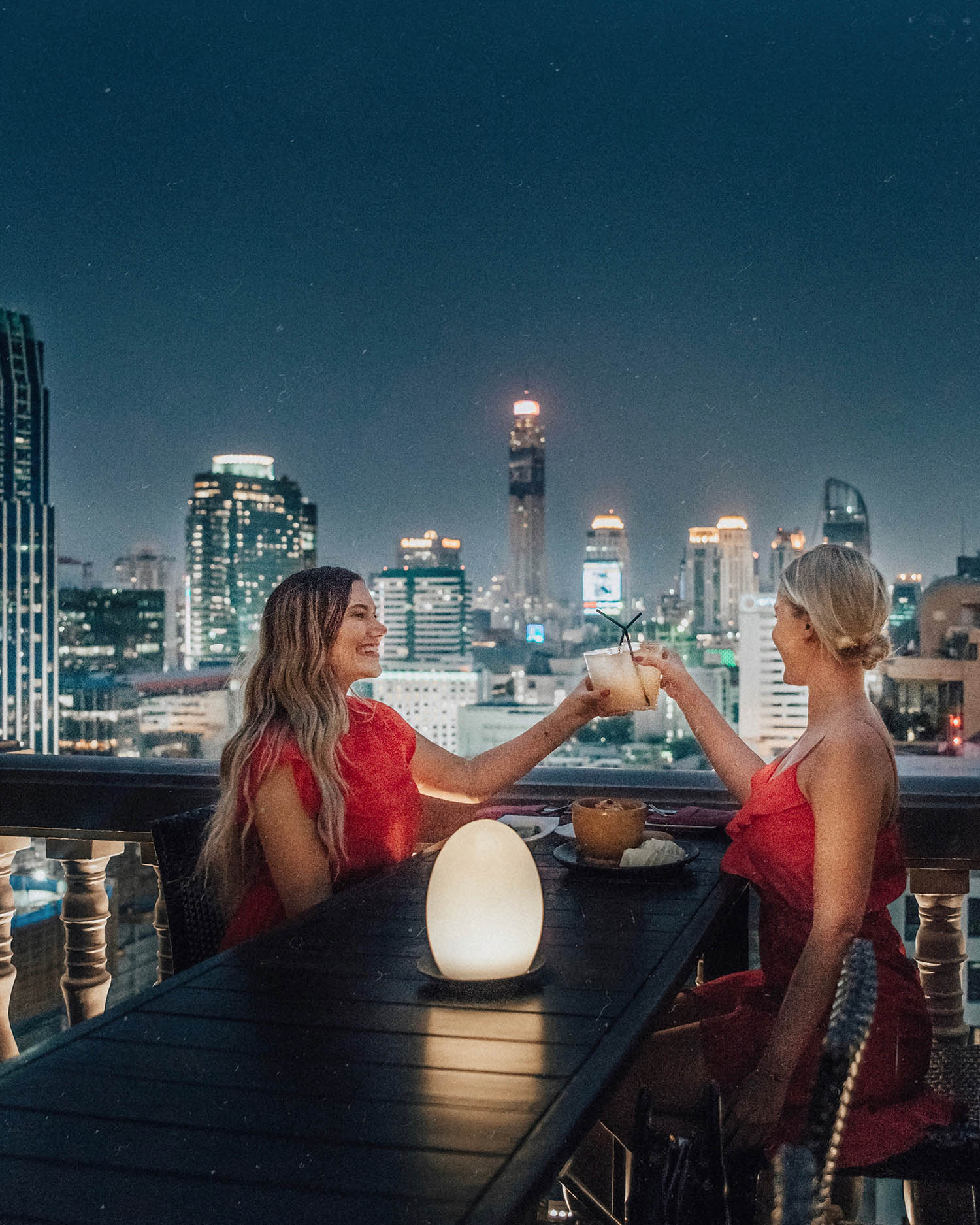 What to Wear in Thailand: Two girls in red dresses sharing a toast - Rooftop Bar at Muse Hotel in Bangkok